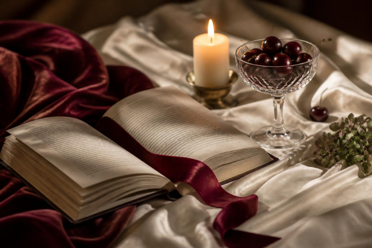 An open spicy romance book on silk sheets beside a candle and cherries